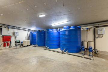 Industrial water treatment and storage facility with large blue tanks, pumps, and a control panel. Clean water supply system and emergency reserve in a technical room or basement.