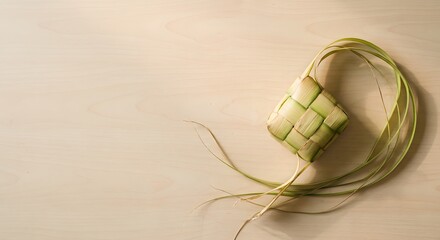 Fototapeta premium Traditional Indonesian Ketupat rice dumpling woven from young coconut leaves on a minimalist wooden table. Natural window light with copy space for Ramadan and Eid Al-Fitr design concepts.