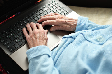 Close-up of an elderly person's hands typing on a laptop keyboard.
