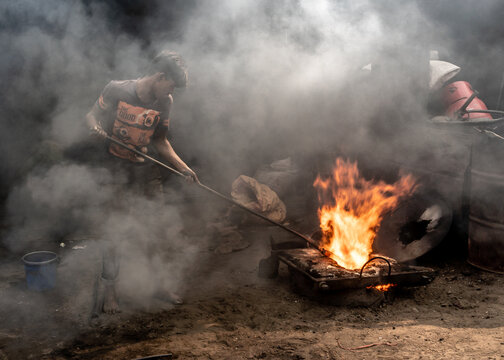 Dhaka, Bangladesh - 12 January 2019: View of a man amidst billowing smoke, tending to a fiery forge, the intense heat contrasting with the gloom.