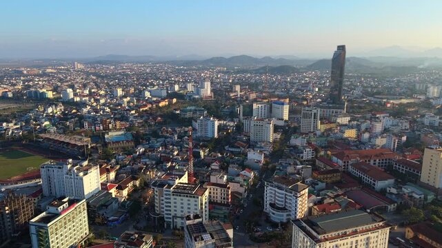 Aerial drone view of Hue city skyline in central Vietnam. Urban landscape with residential buildings, modern high-rise towers and distant mountains during warm sunset light.