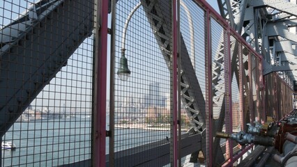 Williamsburg Bridge in Brooklyn, New York City, United States. Transport metallic bridge near Marcy Av subway station and Domino park in Williamsburg. East River and Manhattan view thru pink fence.