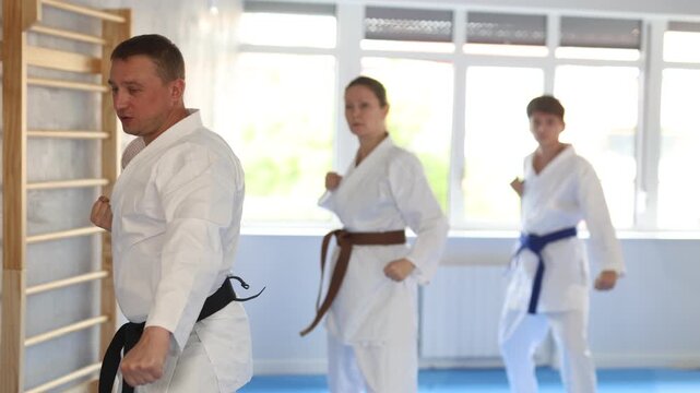 Woman and man in kimono standing in fight stance during group karate training