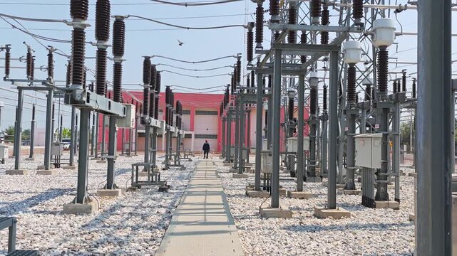 Video of electrical engineer worker walking on path in high voltage power substation switchyard for routine safety inspection and maintenance of electricity distribution grid.