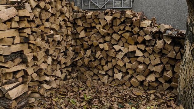 Pile of chopped firewood stacked near wall. Natural brown tones creating rustic countryside atmosphere. Neatly arranged wood logs forming textured pattern. Simple rural scene.