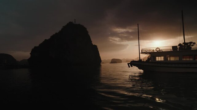 Warm sunset light illuminates calm waters and layered limestone karst silhouettes in Ha Long Bay, Vietnam, creating a tranquil and atmospheric seascape at dusk.