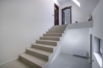 Fototapeta premium Stairs guide the way to a door in a bright hallway. The steps and walls have a light color. The space is open and inviting with minimal decor. Warm light fills the area