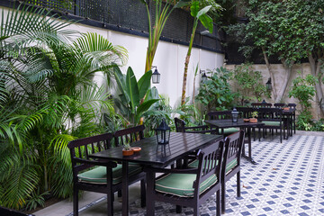 Outdoor cafe patio with black wooden tables and green plants in a tiled courtyard