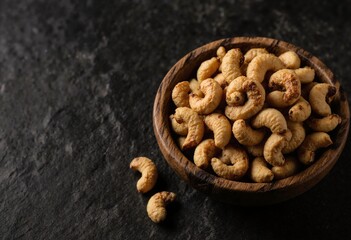 Fototapeta premium Golden roasted cashew nuts served in a rustic wooden bowl on a dark stone background, healthy and crunchy snack