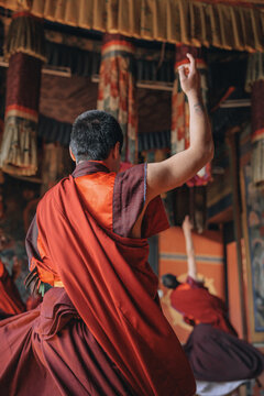 Jakar Dzong, Bhutan - 24 September 2025: View of a monk's raised hand, his flowing crimson robes contrasting with the ornate, textured pillars of the ancient dzong.
