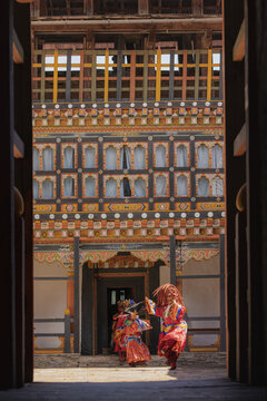 Jakar Dzong, Bhutan - 24 September 2025: View of dancers in vibrant traditional attire performing in front of the ornately decorated Jakar Dzong, a fortress monastery, framed by a dark wooden doorway.