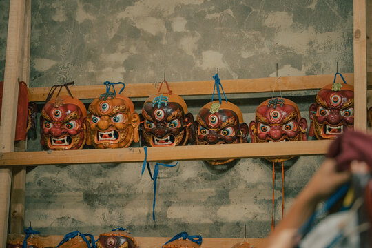 Jakar Dzong, Bhutan - 24 September 2025: View of a row of fierce, vividly colored masks with glaring eyes and snarling expressions, hanging on rustic wooden shelves against a weathered stone wall.