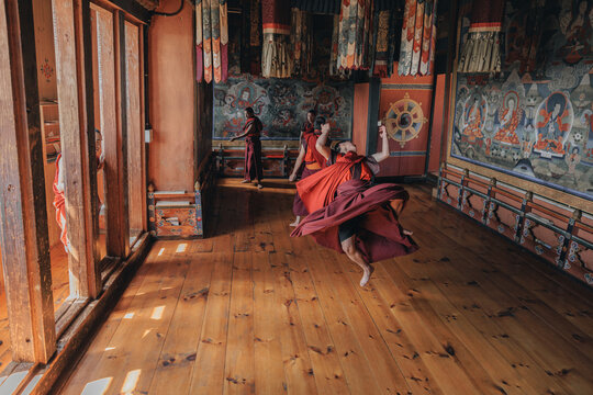 Jakar Dzong, Bhutan - 24 September 2025: View of monks in vibrant red robes dancing and twirling in a sunlit room with painted walls and wooden floors, a blend of tradition and joyous movement.