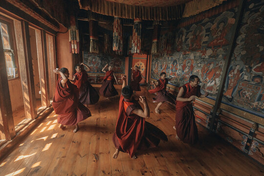 Jakar Dzong, Bhutan - 24 September 2025: View of monks in vibrant red robes moving rhythmically across the wooden floor of a room adorned with detailed murals.