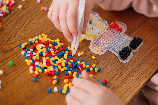 Child's hands using tweezers to assemble a colorful fuse bead mosaic. Creative educational craft activity for kids.