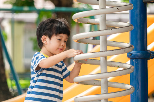 A cute and cheerful little Asian boy as he plays on an outdoor playground. The kid is laughing heartily while enjoying the activities in a public park, a genuine moment of happy childhood