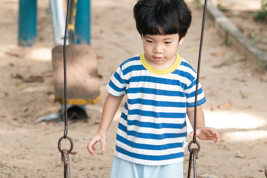 A cute and cheerful little Asian boy as he plays on an outdoor playground. The kid is laughing heartily while enjoying the activities in a public park, a genuine moment of happy childhood