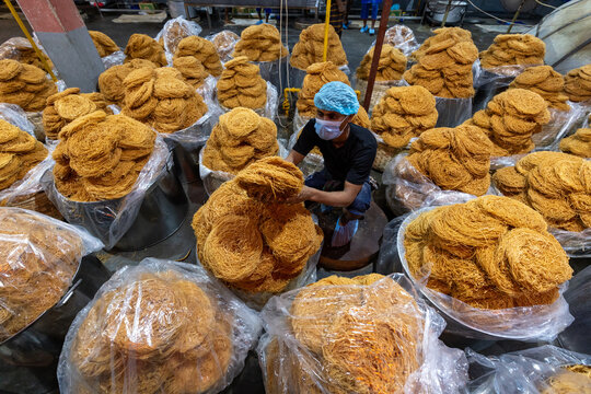 Bogura, Bangladesh - 17 April 2022: View of a worker surrounded by piles of golden vermicelli, their textures contrasting against the sterile plastic wrap, creating a scene of vibrant industry.