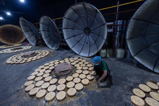 Bogura, Bangladesh - 17 April 2022: View of a worker amidst the soft glow of earthen ovens, crafting golden discs under the watchful eyes of giant, metallic woks.