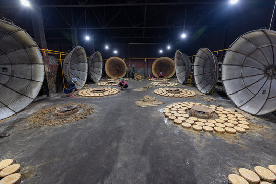 Bogura, Bangladesh - 17 April 2022: View of workers meticulously arranging round, flat dough portions on a dark surface under the dim glow of industrial lighting, next to large, open oven lids.