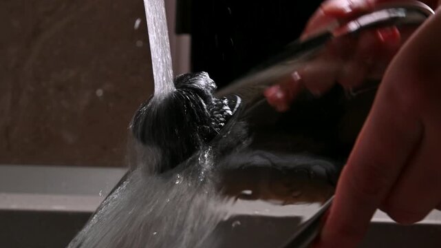 Close-up of hand lifting a pot lid as water cascades from the edge, showcasing the flow of water in a kitchen setting with a modern aesthetic