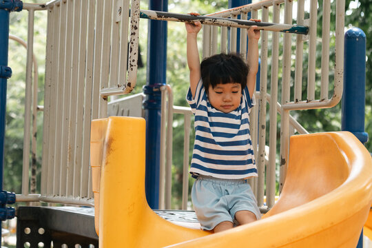 A portrait of a cute and cheerful little Asian boy as he plays on an outdoor playground. The kid is laughing heartily as they enjoy the Slide in a public park, a genuine moment of happy childhood.