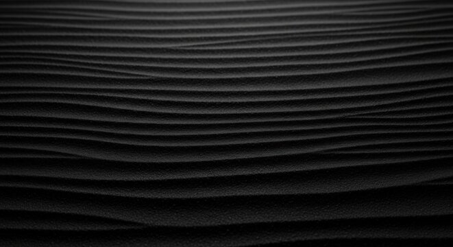 Monochromatic close-up showing dark, undulating sand ripples creating a dramatic black background texture.