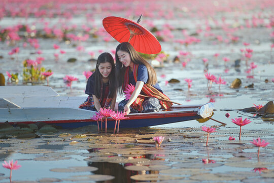 Two young women sitting in a boat holding a traditional parasol looking at pink water lilies, Red Lotus Sea (Talay Bua Daeng), Udon Thani, Northeast Thailand, Thailand
