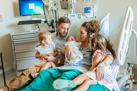 Woman sitting in a hospital bed with her husband and two children holding her newborn son