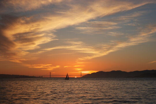 Distant silhouette of a sailboat sailing pas the Golden Gate Bridge at sunset, San Francisco, California, USA