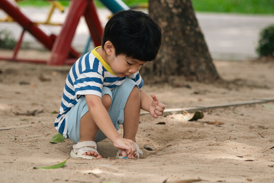 A portrait of a cute and cheerful little Asian boy as he plays on an outdoor playground. The kid is laughing heartily as they enjoy the sand in a public park, a genuine moment of happy childhood.