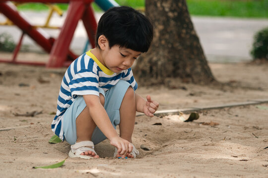 A portrait of a cute and cheerful little Asian boy as he plays on an outdoor playground. The kid is laughing heartily as they enjoy the sand in a public park, a genuine moment of happy childhood.