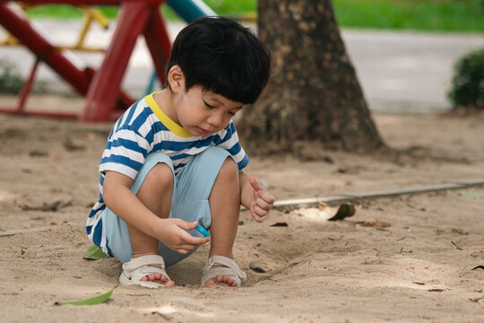 A portrait of a cute and cheerful little Asian boy as he plays on an outdoor playground. The kid is laughing heartily as they enjoy the sand in a public park, a genuine moment of happy childhood.