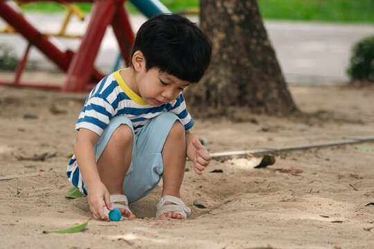 A portrait of a cute and cheerful little Asian boy as he plays on an outdoor playground. The kid is laughing heartily as they enjoy the sand in a public park, a genuine moment of happy childhood.