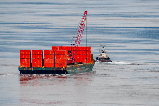 Tug towing a barge with red containers between islands near Campbell River, British Columbia, Canada