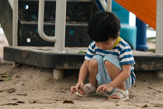 A portrait of a cute and cheerful little Asian boy as he plays on an outdoor playground. The kid is laughing heartily as they enjoy the sand in a public park, a genuine moment of happy childhood.