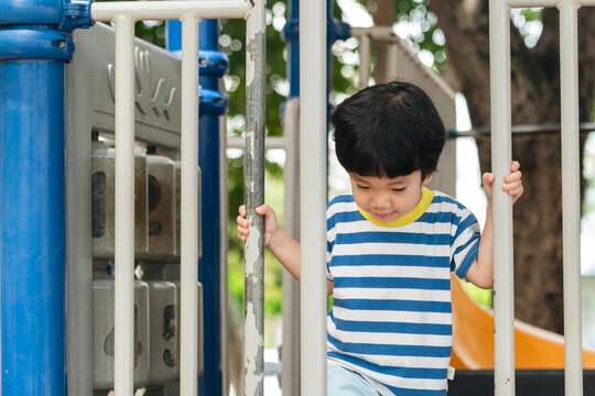 A cute and cheerful little Asian boy as he plays on an outdoor playground. The kid is laughing heartily while enjoying the activities in a public park, a genuine moment of happy childhood