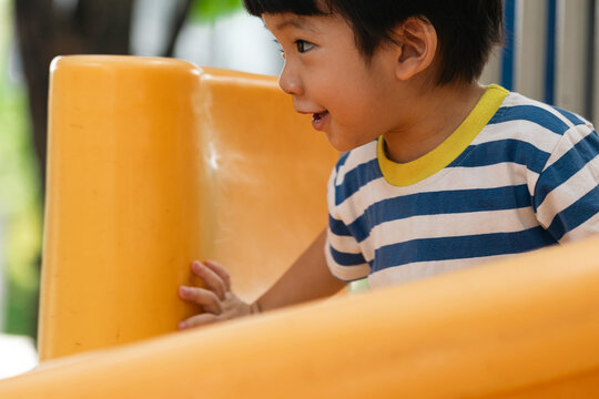 A portrait of a cute and cheerful little Asian boy as he plays on an outdoor playground. The kid is laughing heartily as they enjoy the Slide in a public park, a genuine moment of happy childhood.