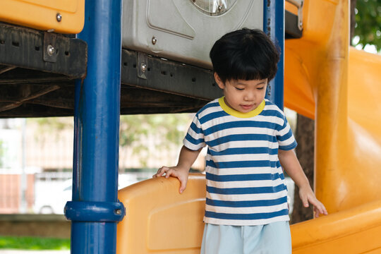 A cute and cheerful little Asian boy as he plays on an outdoor playground. The kid is laughing heartily while enjoying the activities in a public park, a genuine moment of happy childhood