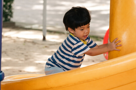 A portrait of a cute and cheerful little Asian boy as he plays on an outdoor playground. The kid is laughing heartily as they enjoy the Slide in a public park, a genuine moment of happy childhood.