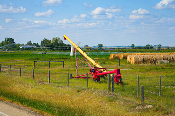 Grain auger and hay bales on a summer farm field in Alberta, Canada