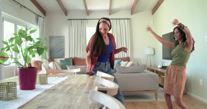 Diverse women friends entering open living room, seeing phone on table, unlocking phone and dancing