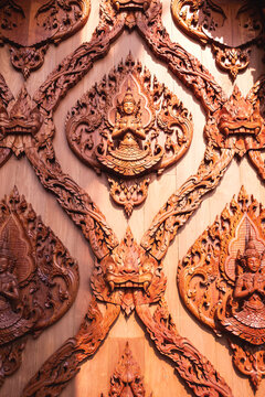 Intricate Thai wood carving of Thepanom angel with traditional Kanok patterns on teak wooden temple wall in vertical frame, showcasing exquisite Asian craftsmanship and cultural heritage.