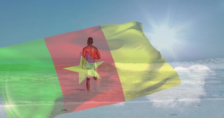Naklejka premium Walking surfer carrying surfboard and wearing swim trunks into shallow ocean at beach, flag overlay