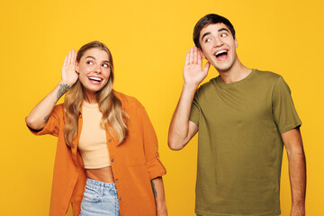 Young curious nosy couple two friends family man woman wear casual clothes try to hear you overhear listening intently together isolated on pastel plain light yellow color background studio portrait.