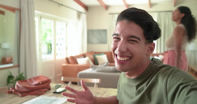 Couple in living room, camera recording man presenting at table while woman entering with suitcase