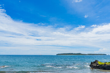 Obraz premium Beautiful tropical beach with blue ocean waves, rocky coastline, and a distant green island under a bright sunny sky in Bengkulu, Indonesia.