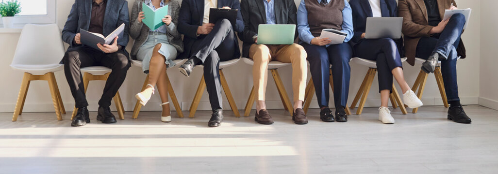 Candidates waiting interview with resumes for hiring. People on chairs using laptops in a bright office lobby awaiting team review and job tests. Symbol of recruitment and hiring process.