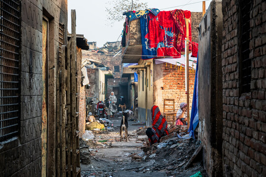 Dhaka, Bangladesh - 28 November 2025: View of a narrow alleyway where shadows dance between dilapidated buildings and colorful fabrics hang overhead, hinting at life amidst the decay.