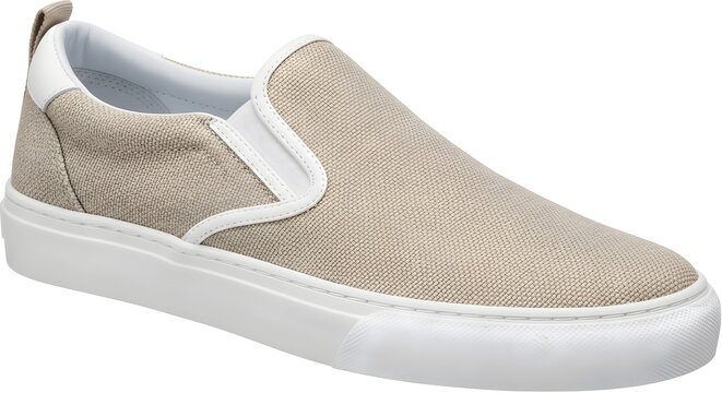 Close up beige canvas slip on sneaker angled three quarter view showing textured upper white rubber sole elastic gore pull tab on white background studio lighting